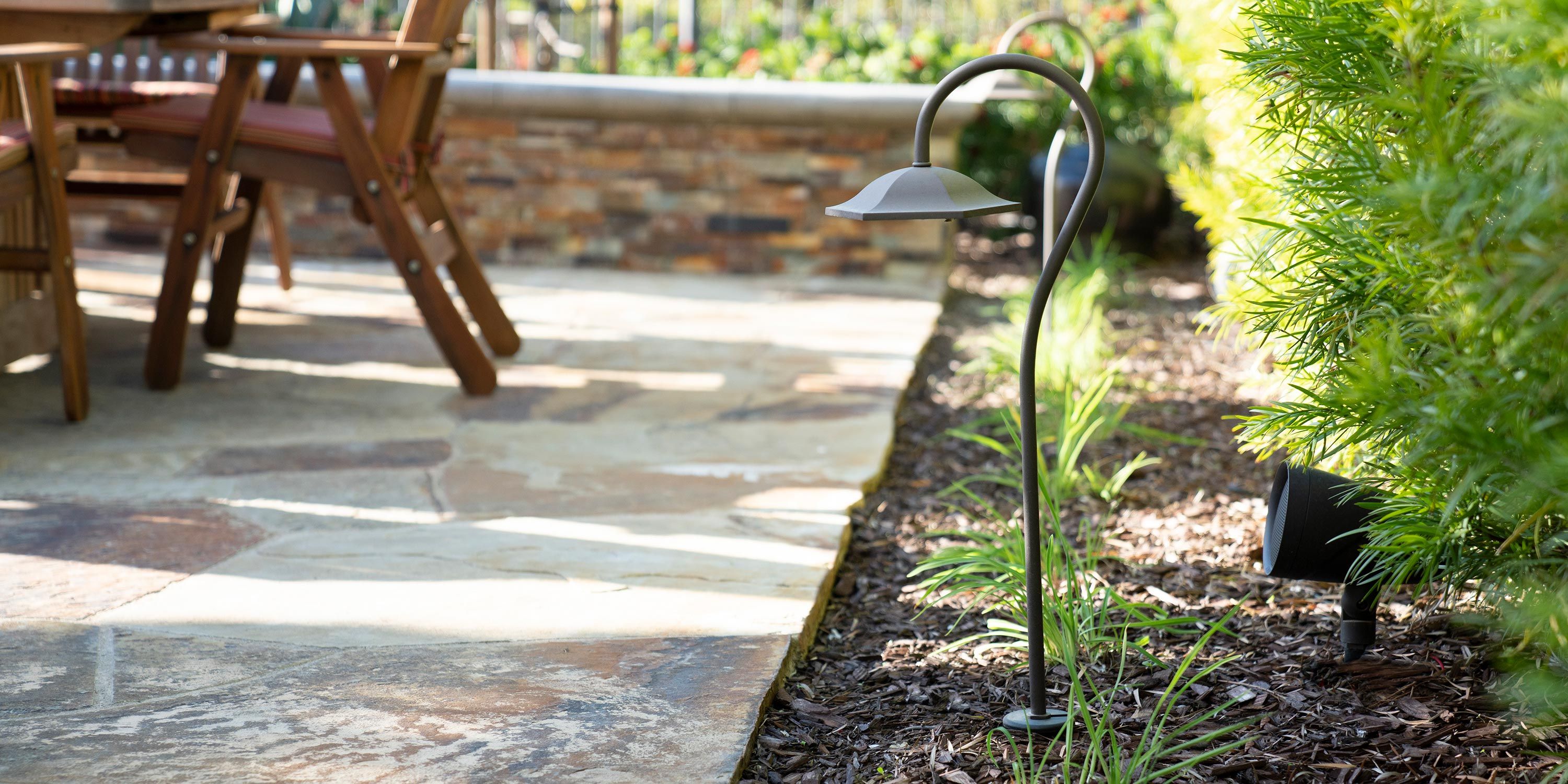 An outdoor scene featuring a path with a garden light and a wooden dining set in the background.