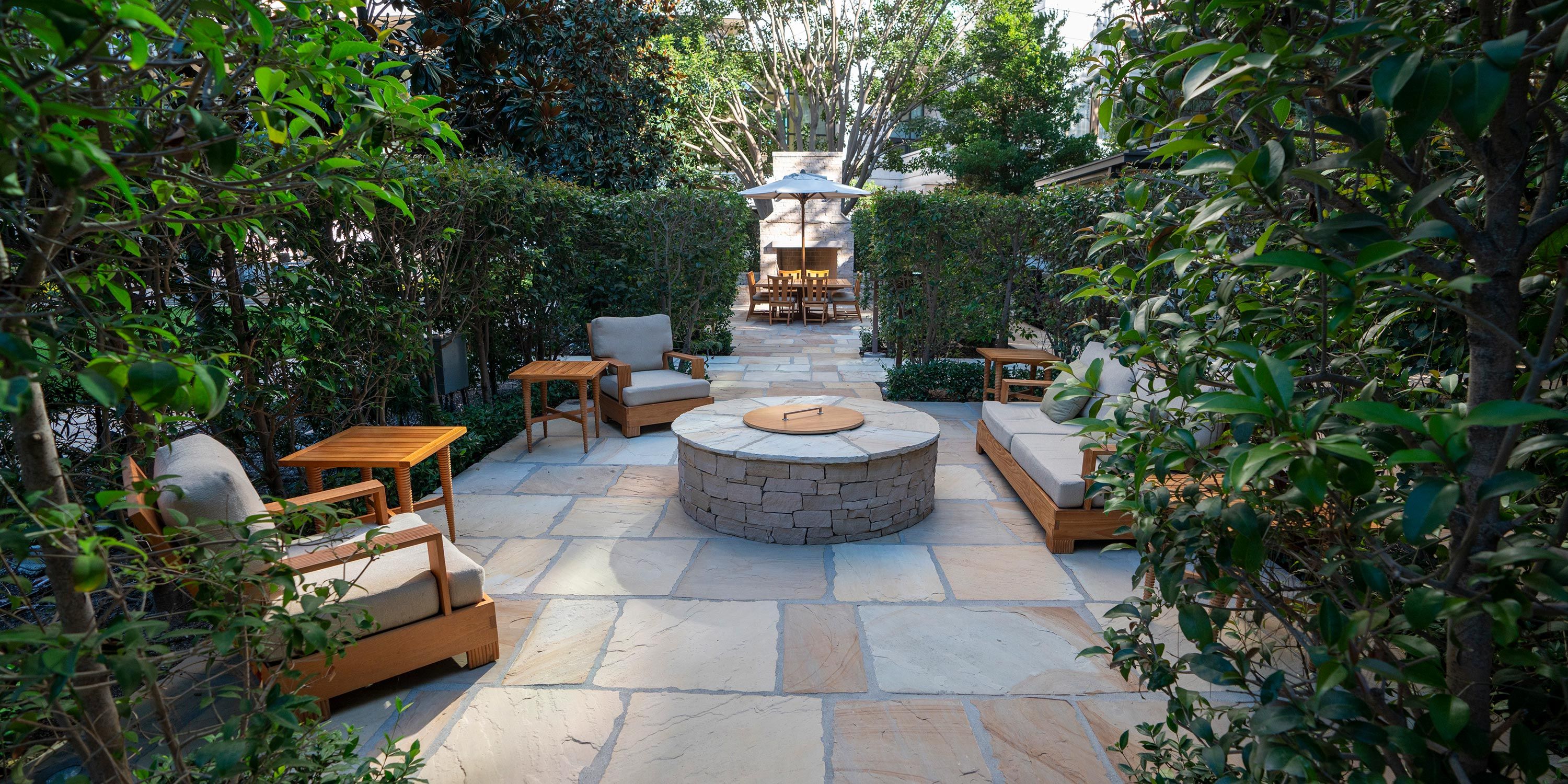 A private garden patio with cushioned chairs, a central fire pit, and surrounding hedges providing seclusion.